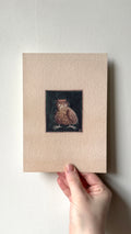 'The King' print held in a hand: a small brown owl-like creature in a crown on a dark background