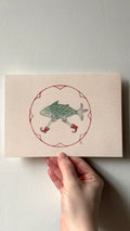 'Fish' print held in a hand: a green scaled fish on two legs in red boots, inside a red circle