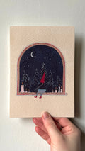 'Winter Creacher' print held in a hand: a creacher in red by an arched window, night sky, moon and snowy pines