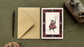 "Lightbearer" greetings card with a brown envelope: a cloaked creacher carrying a branch of lit candles