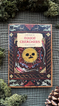 'Goode Creachers Bestiary' zine cover: a gold sun face in a patterned frame, laid on moss with pine cones