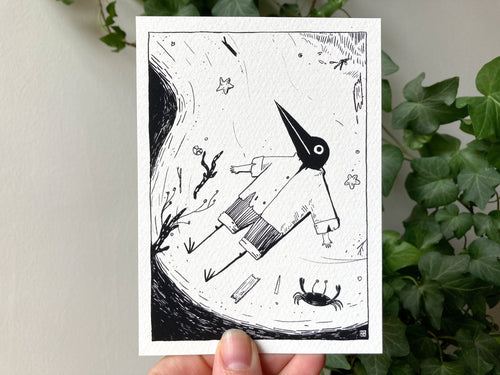 "Beached" print held in a hand: ink drawing of Birdface lying flat on the sand beside a starfish and a crab