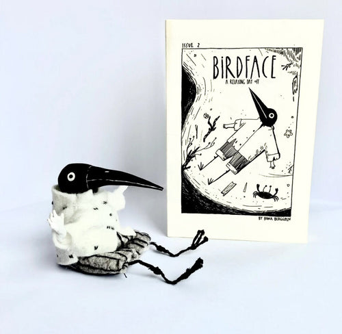 "Birdface: Issue 2" zine standing beside a small handmade Birdface figure with a black beak