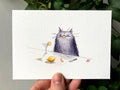 "Sour" print held in a hand: a fluffy grey cat at a table with lemons and a martini glass