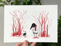 "Winter Walk" print held in a hand: Birdface in a red scarf meets a small ratbag among bare red winter trees
