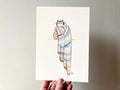 "Blanket Cat" print held in a hand: a tabby cat wrapped in a striped blanket
