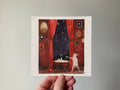 "The Ghost" print held in a hand: a white ghostly figure by a table with a teacup, framed by red curtains