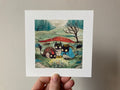 "The Swamp Kids" print held in a hand: three small black cat-like creatures by a swamp under a red tree