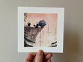 "Pim & Pom" print held in a hand: two small black creatures pushing a cauldron off a cliff edge