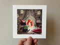 "Soren Spider-Stealer II" print held in a hand: Soren in a red hat reading beside a fire in a tree hollow