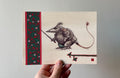 "The Knight" print held in a hand: Ser Metle, a small armoured creature with a long tail, holding a sword