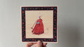 "The Trumpeter" print held in a hand: a white hare-like figure in a red robe with a trumpet, in a flowered border