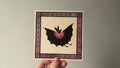 "The Night Prince" print held in a hand: a black bat-like creature with a pink ruff inside a purple border