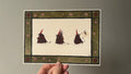 "The Undercreachers" print held in a hand: three small dark creatures in red pointed hats walking in a line